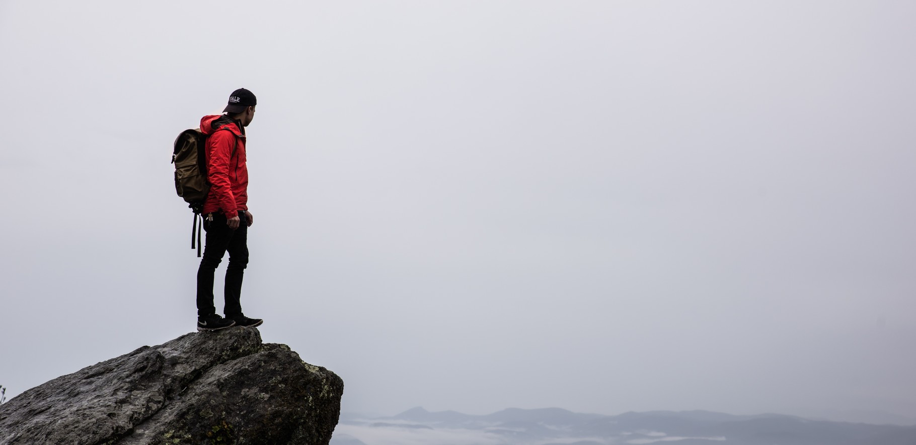 Tramper with a backpack on standing on the edge of a rock over looking a valley