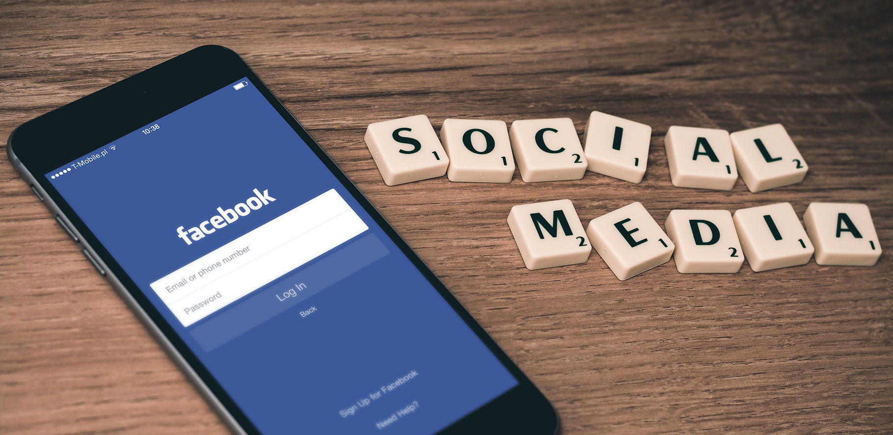 A phone with facebook on the screen is sitting on a desk with the words social media spelled out in scrabble titles sitting next to it