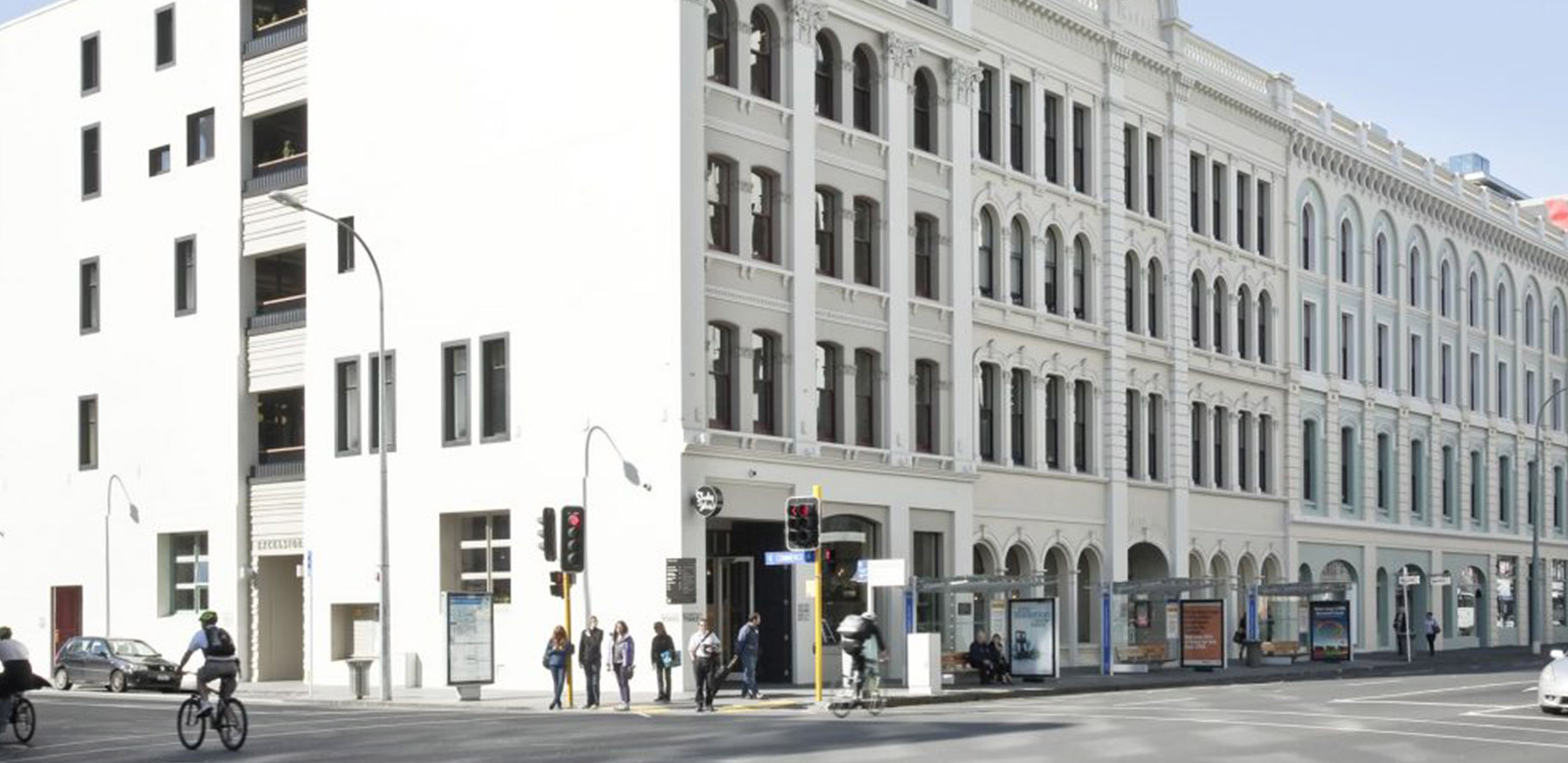 people standing on a street corner waiting for the lights with a big building behind them