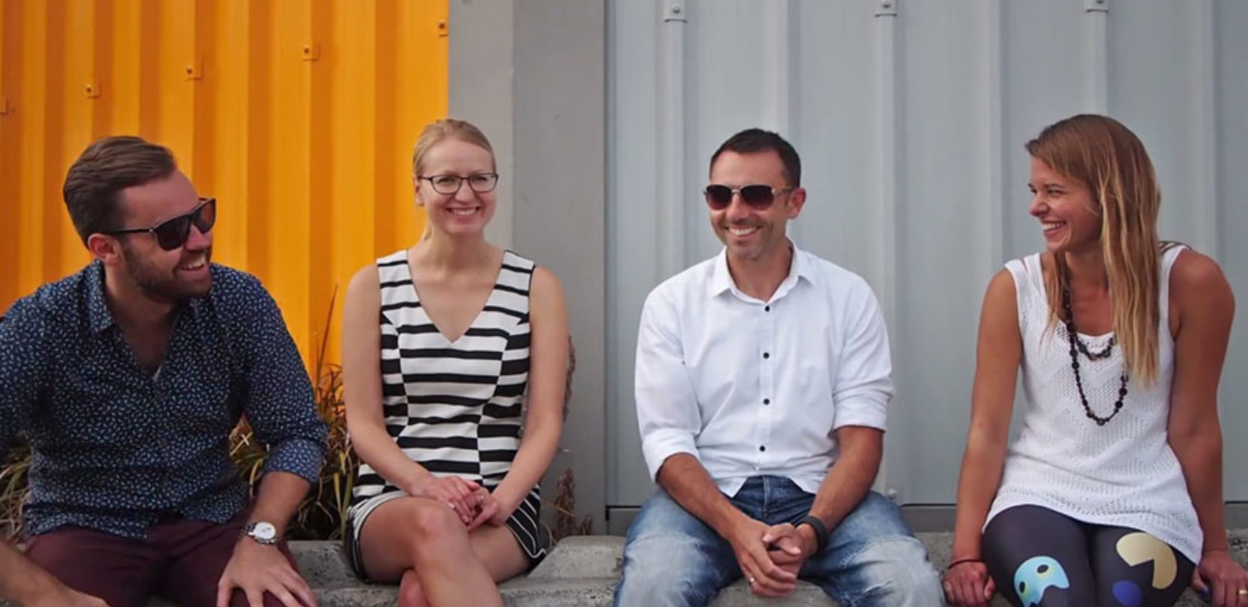 group of 4 people sitting down in an industril area talking and smiling.