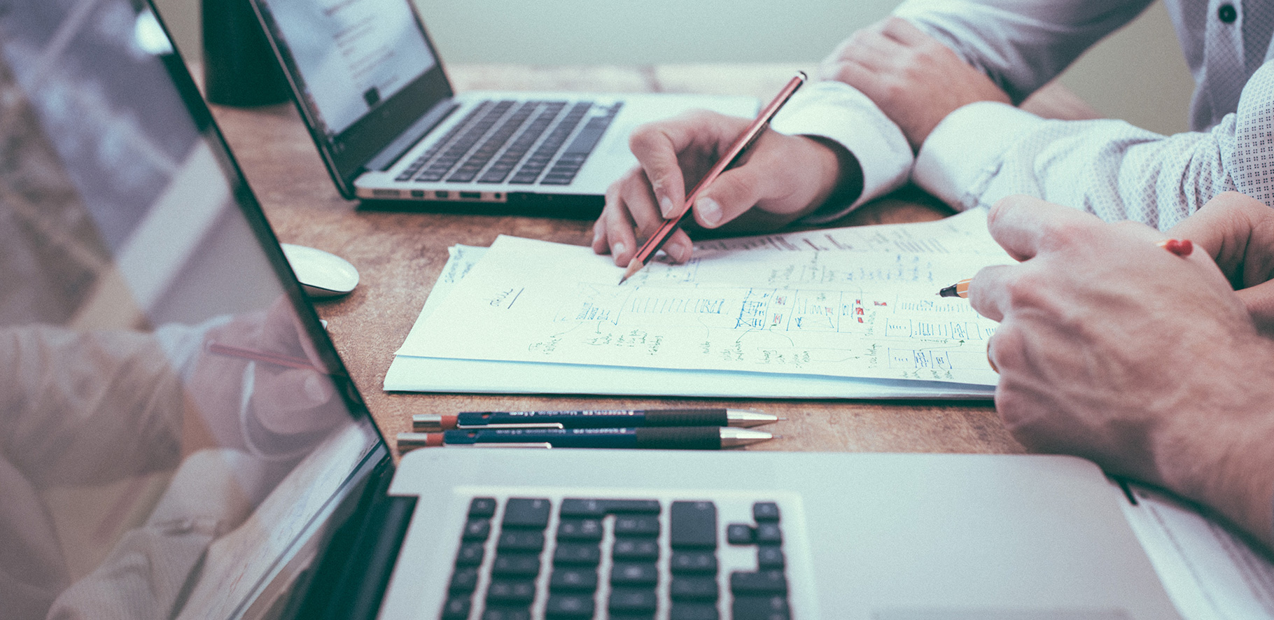two people sitting at a table with their laptops discussing documents