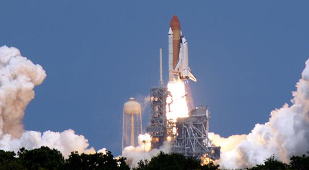 A rocket is at the begining stages of being launched into space with burners firing and smoke billowing out from the bottom