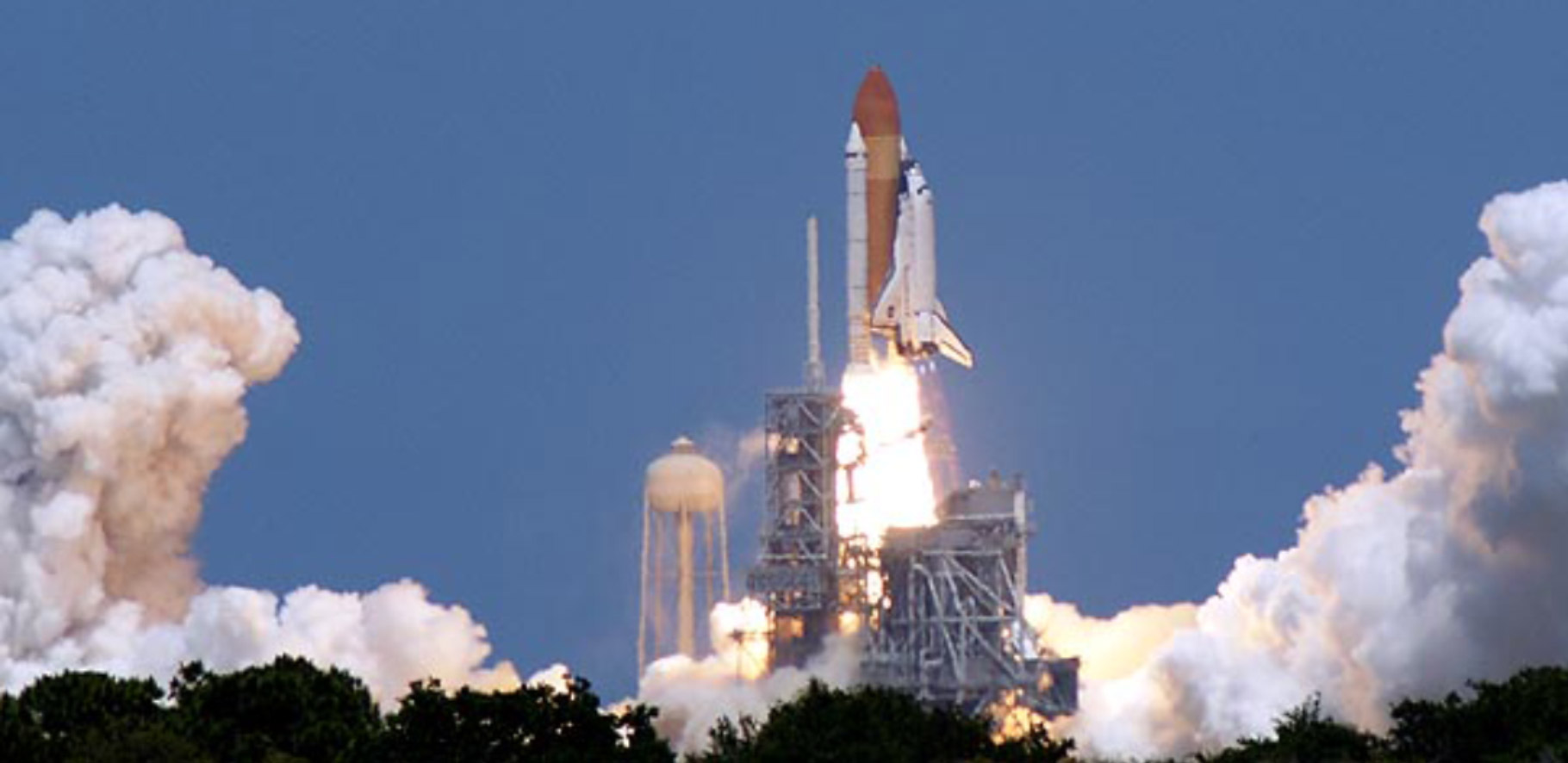 A rocket is at the begining stages of being launched into space with burners firing and smoke billowing out from the bottom