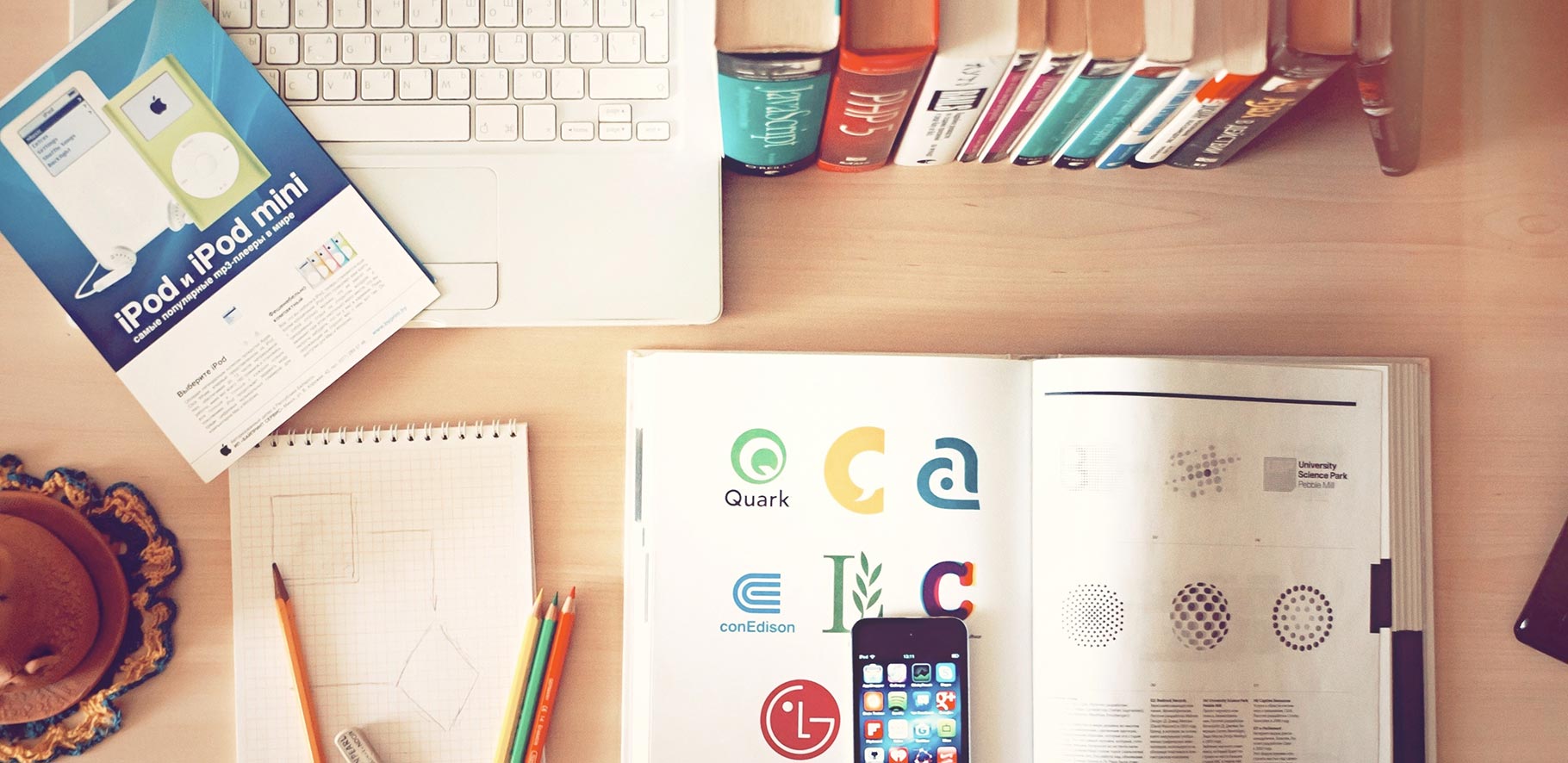 looking down onto an office desk which shows a lap, notepad, pencils, phone and an open book